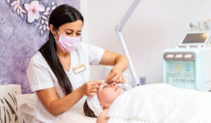 A cosmetologist in a medical mask does a facial massage procedure for a client.